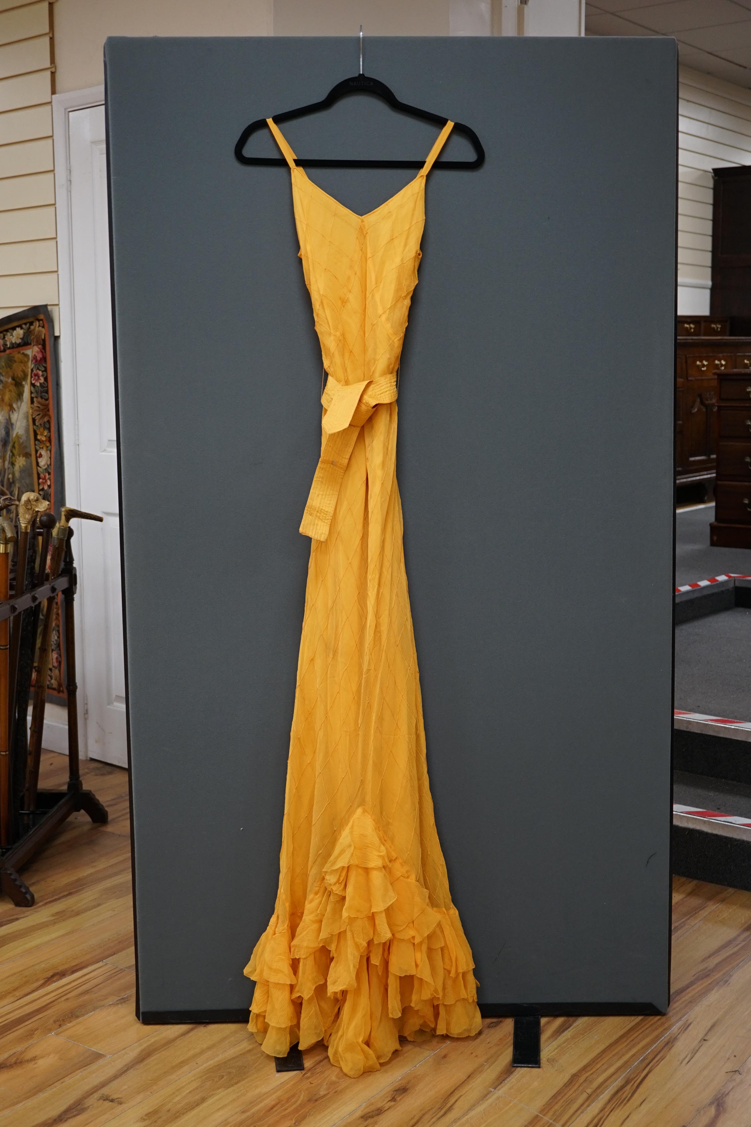 A 1930’s Harrods labelled saffron silk chiffon evening dress and jabot, lined in the same coloured taffeta, the dress kipper shaped with thin camisole straps and the chiffon sewn on the bias in diagonal seams finished wi